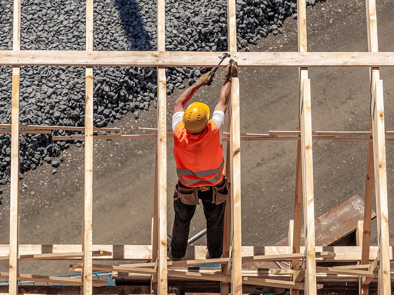 A builder nailing wooden forms over a gravel base before a concrete pour